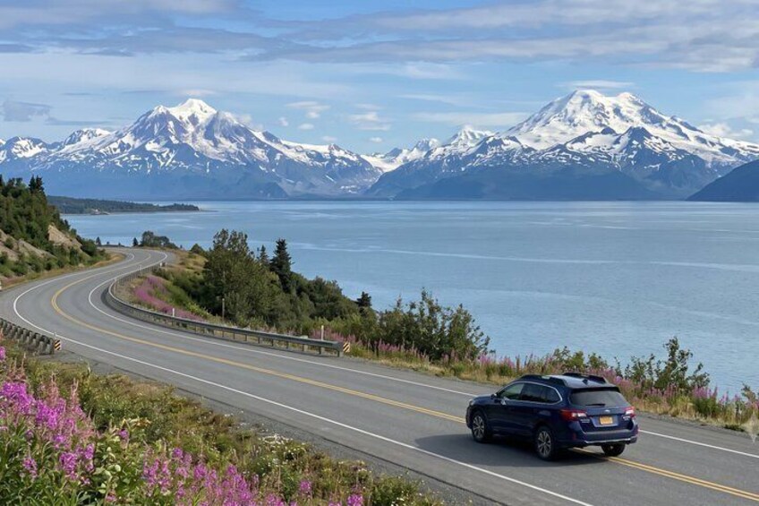 A winding road with a car, mountains, and a body of water. 1