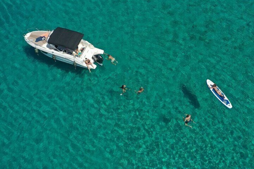 A boat with people on a turquoise sea, a smaller boat nearby, and a person on a paddleboard. 1