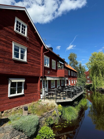 A red wooden building with white windows, a dock extending over a calm river, and greenery along the riverbank. 5