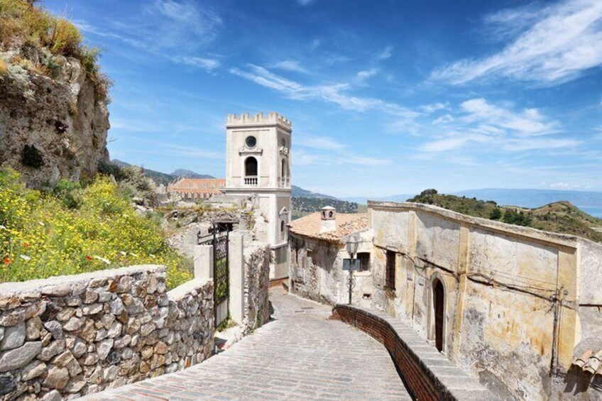 A stone pathway leading to a tower, surrounded by rocky terrain and buildings. 5