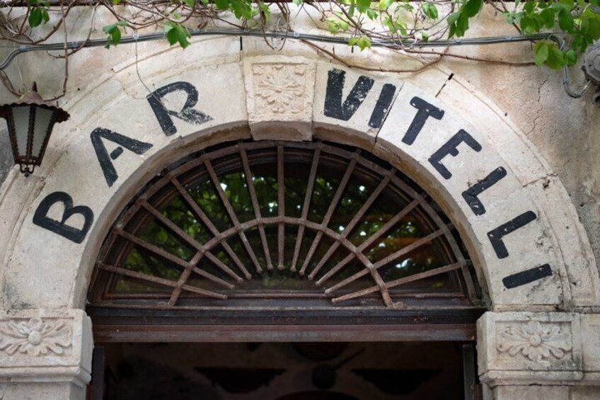 An arched entrance with the words 'BAR VITELLI' carved into the stone. 4