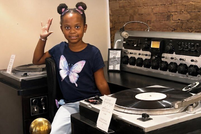 A person sitting at a turntable with vinyl records, a mixer, and a gold speaker. 4