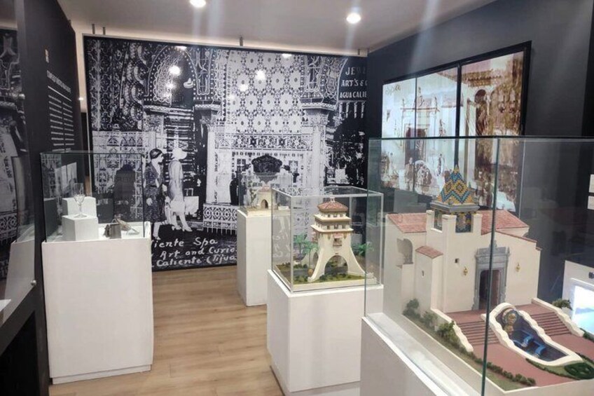A museum interior with glass display cases, a model of a building, and a patterned wall. 3