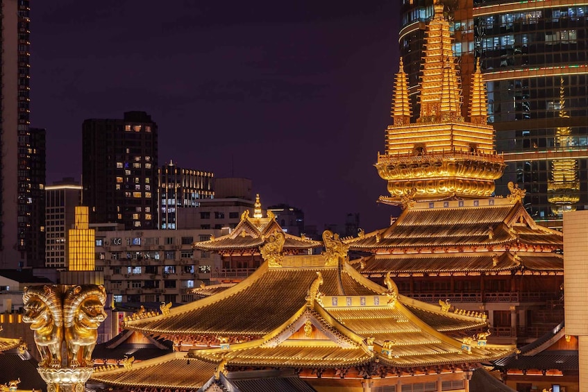 A traditional temple with golden roofs and statues, set against a modern cityscape at night. 1