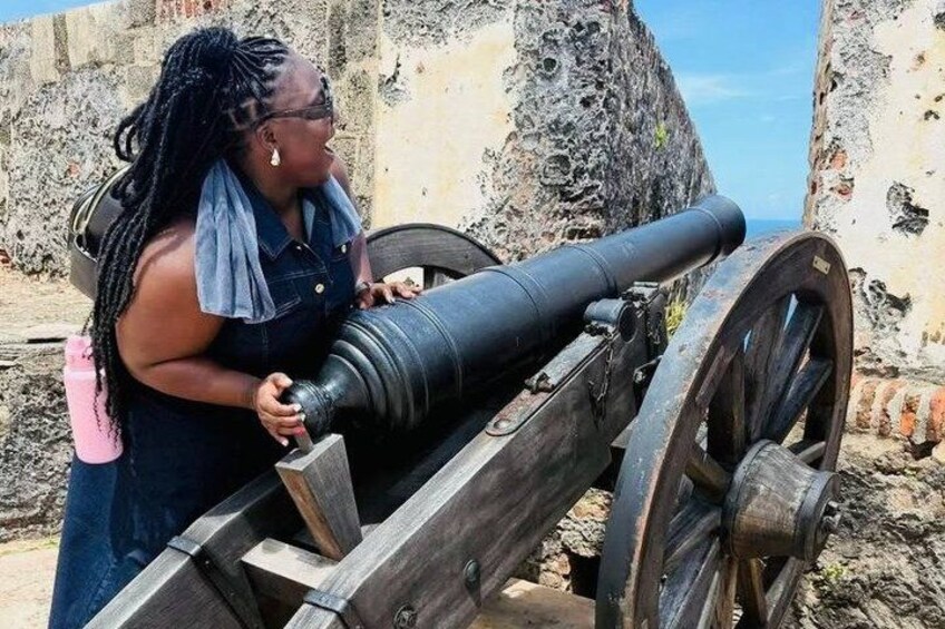 A person operating a cannon on a historic site with rocky terrain and a clear sky. 2