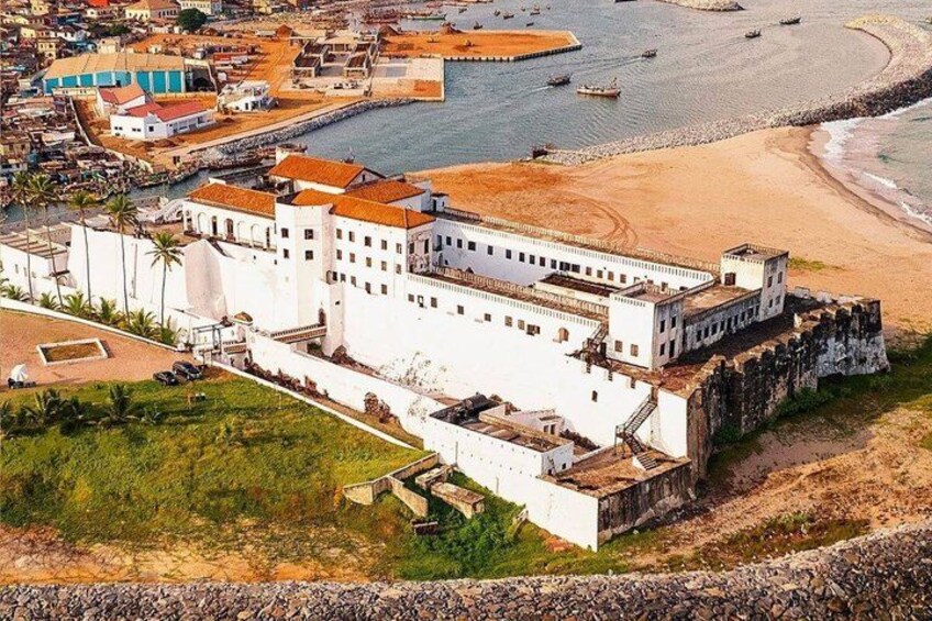 A coastal fortification with a large white building, a sandy beach, and a calm sea. 1