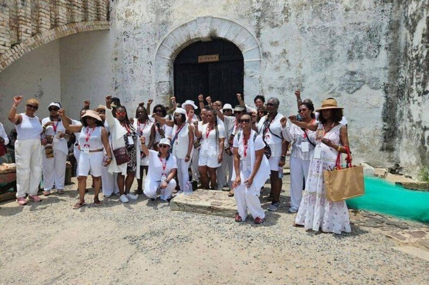 A group of people in white attire posing in front of a historic building with a green roof. 4