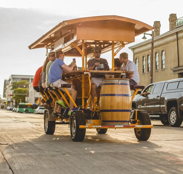 A group of people riding a wooden cart with a barrel attached, on a city street. 2