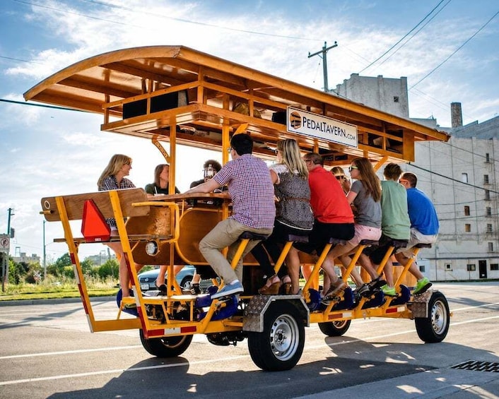 A yellow trolley with passengers, labeled 'PEDALTAVERN.COM,' on a road. 1