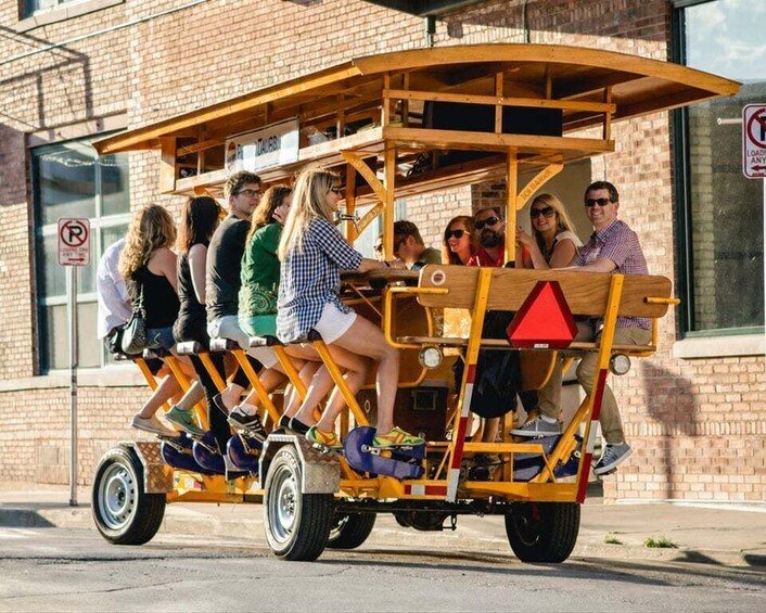 A group of people riding a wooden cart with a triangular front and wheels, parked on a street with a brick building and a 'No Parking' sign in the background. 3