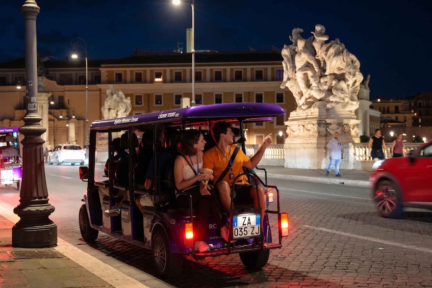 A purple tour vehicle parked on a cobblestone street with a large statue in the background. 2