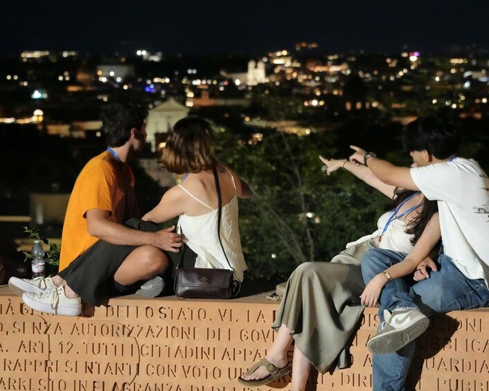 Three people sitting on a ledge with a cityscape in the background. 4
