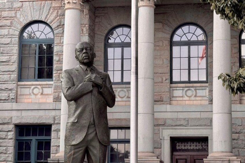 A statue of a man in a suit standing in front of a building with large columns and arched windows. 4