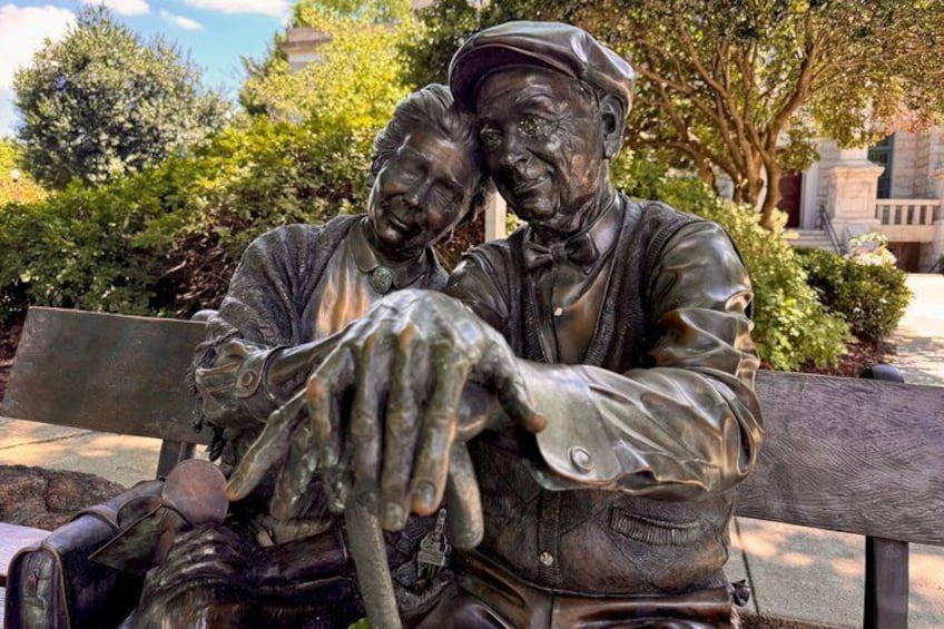 A bronze statue of two men sitting on a bench in a park. 5