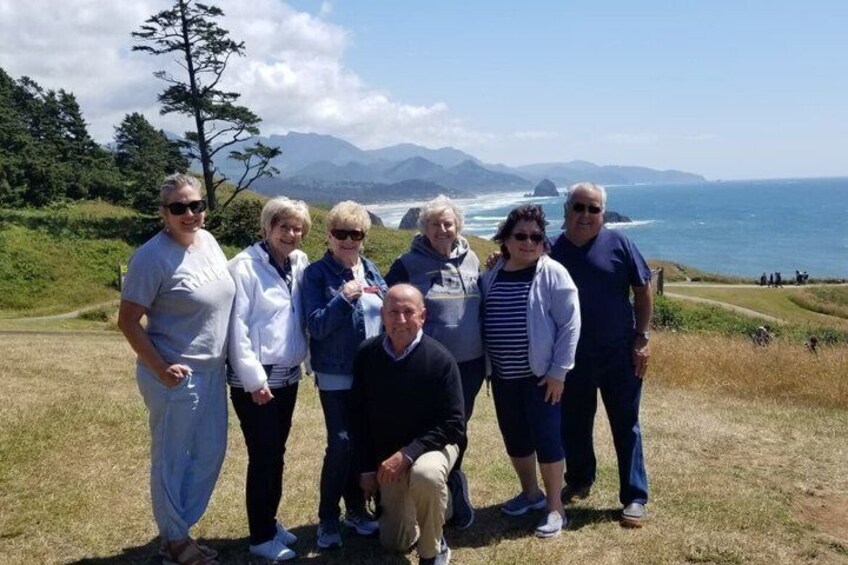 A group of people standing on a grassy hill overlooking a coastal landscape with mountains in the distance. 2