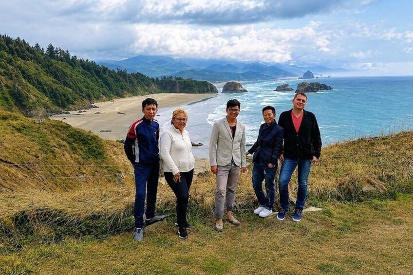 A group of people standing on a grassy hill overlooking a beach and ocean. 1