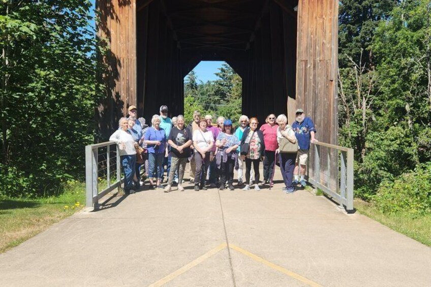 A group of people standing under a wooden covered bridge. 2
