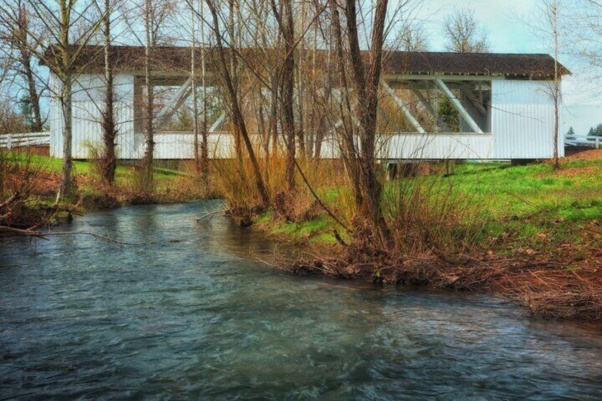 A white building with a metal roof near a flowing river, surrounded by trees and grass. 5