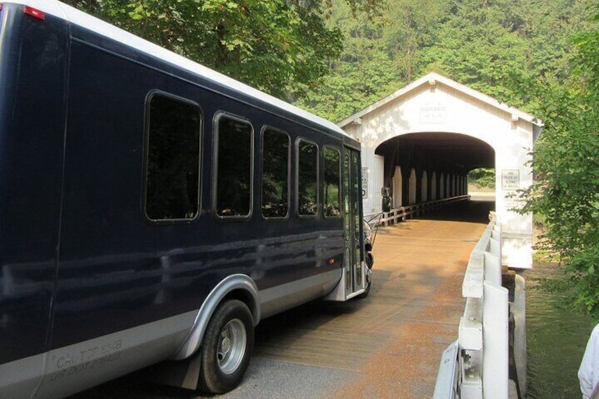 A bus parked at a covered bridge with a forested area in the background. 4