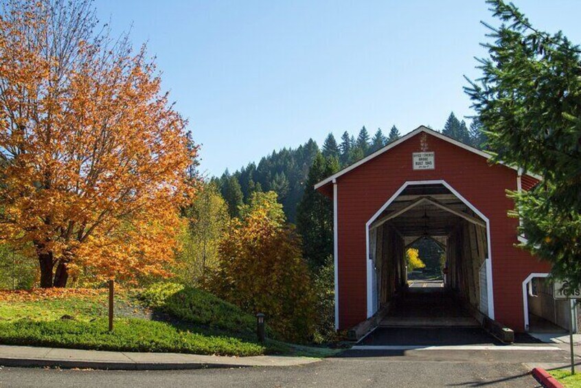 A red covered bridge with a sign, surrounded by autumn trees and a forested background. 3