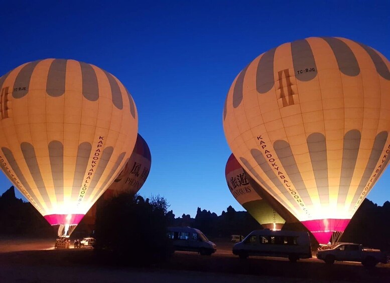 Two hot air balloons with 'KAPADOKYABALLOO' written on them, parked on a road with vehicles around. 2