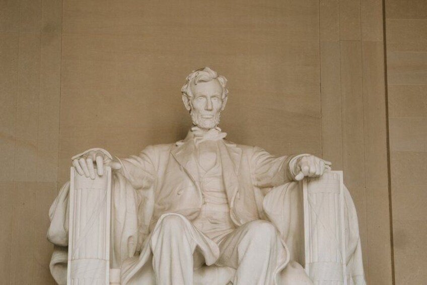 A marble statue of a seated man with outstretched arms, wearing a suit and tie. 3