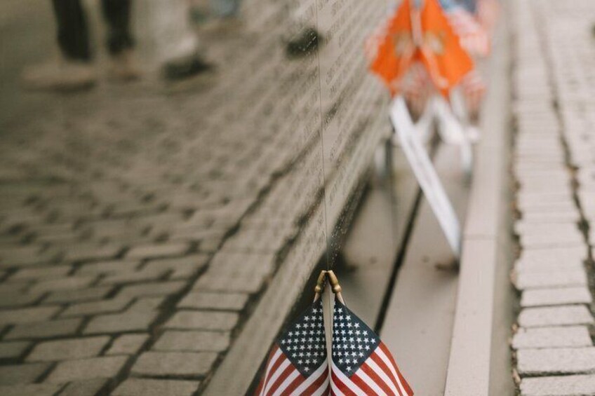A sidewalk with a patterned brick surface, a metal fence, and a small American flag hanging from a string. 5