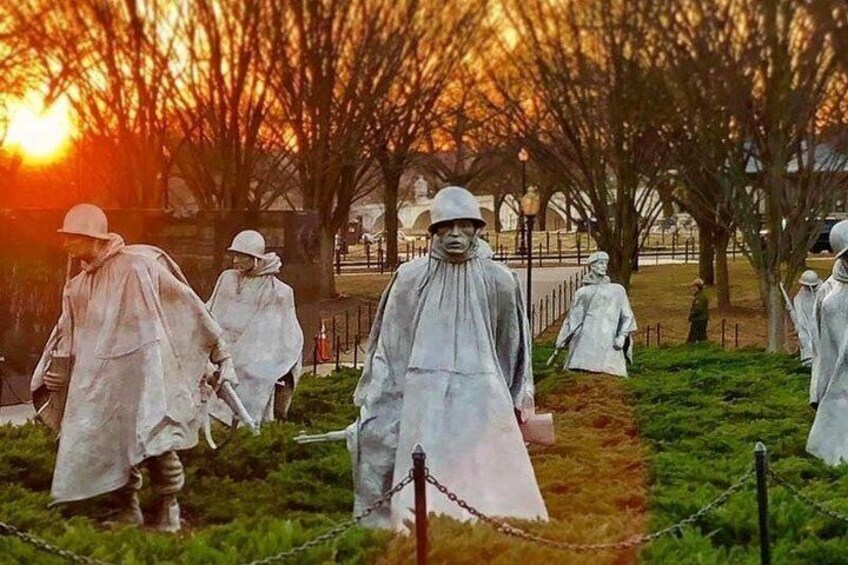 A statue of a person in a raincoat and hat, surrounded by similar statues in a park. 2