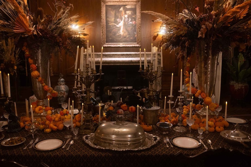 A formal dining table set with candles, pumpkins, and a silver platter. 4