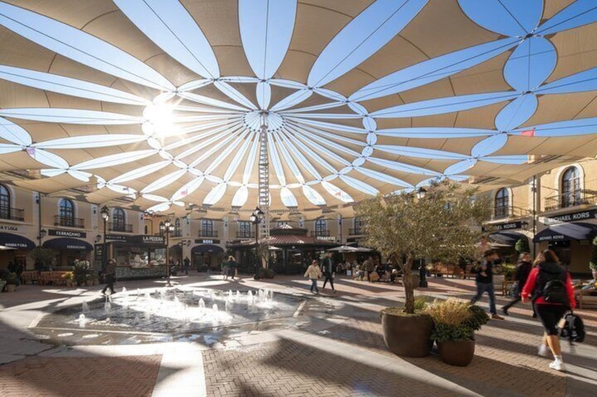 A plaza with a fountain, potted plants, and people walking. 3