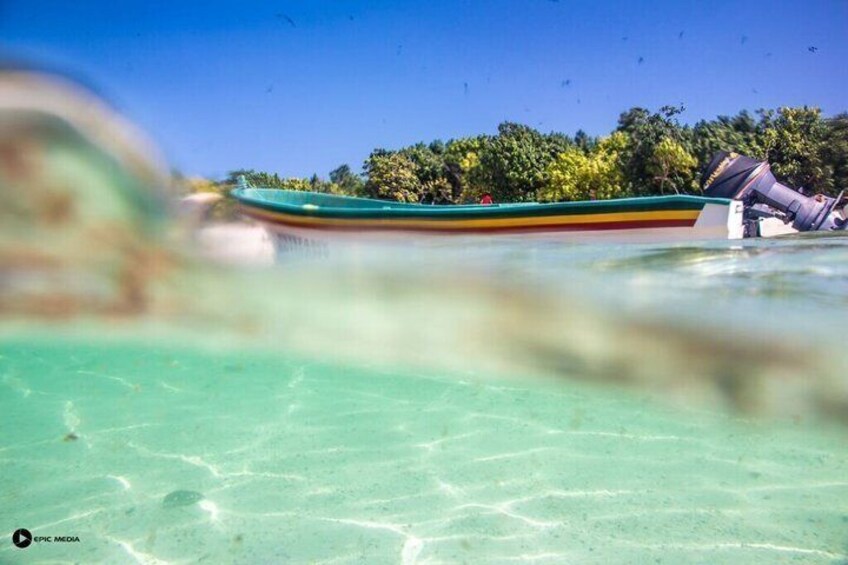 A boat on clear turquoise water with a forested island in the background. 1