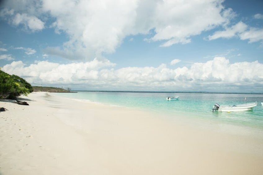 A beach with clear turquoise water, a sandy shore, and a few small boats. 4