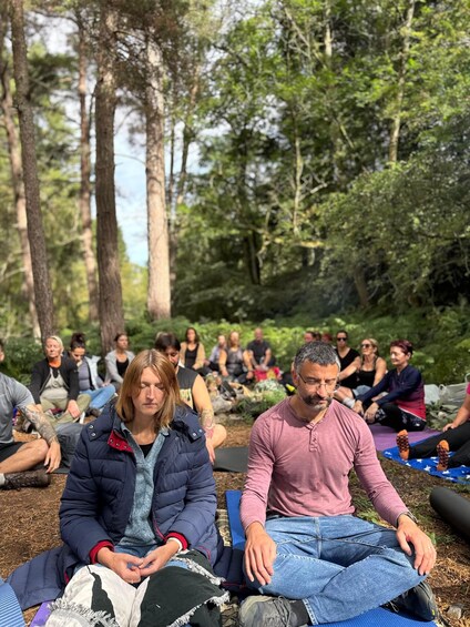 A group of people sitting on mats outdoors in a forested area. 5