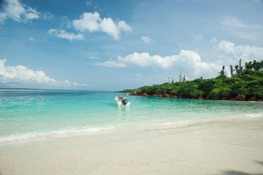 A beach with clear turquoise water, a small boat, and a rocky outcrop with vegetation. 5