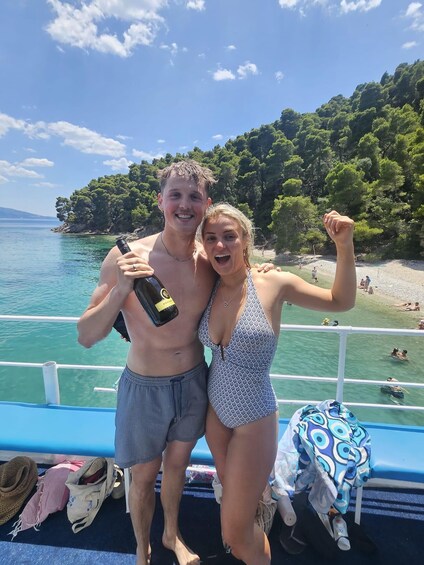 Two people on a boat, a bottle of Prosecco, and a beach with people in the background. 4