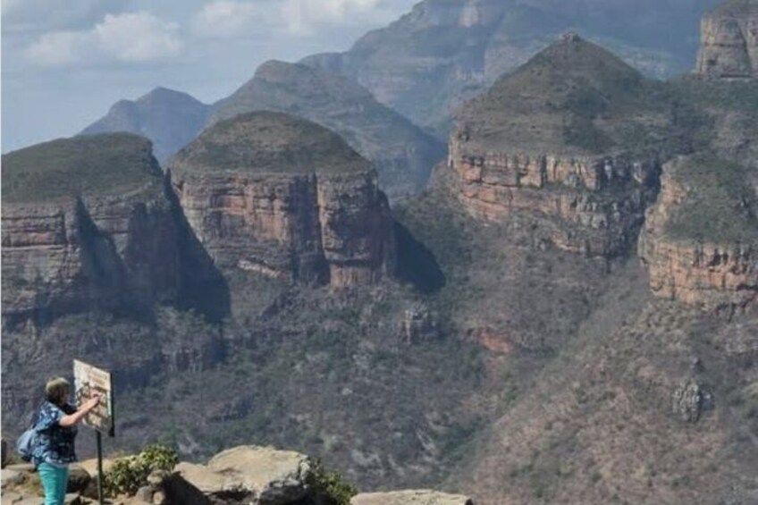 Eine Person malt eine Landschaft mit einem tiefen Canyon, steilen Klippen und spärlicher Vegetation. 2