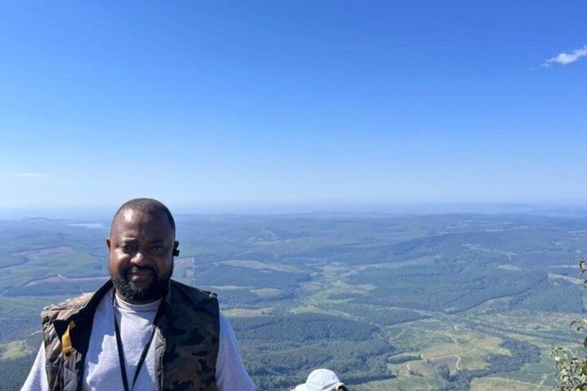 Eine Person steht auf einer erhöhten Aussichtsplattform und blickt auf eine weitläufige Landschaft mit sanften Hügeln und blauem Himmel. 5