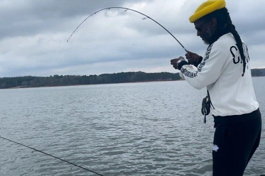 A person fishing on a boat with a lake and a forested shoreline in the background. 1