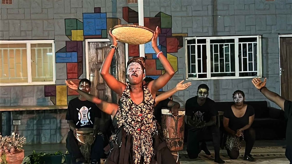 A person balancing a large object on their head, surrounded by others. 3