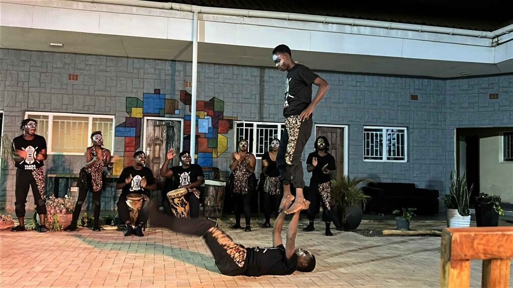 A group performing acrobatics in front of a building with colorful geometric patterns. 1
