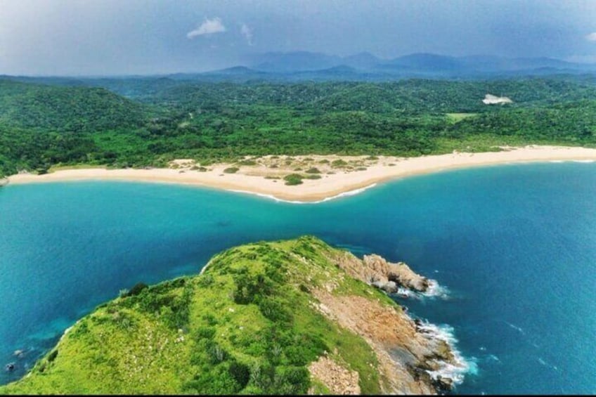 A coastal landscape with a beach, green hills, and a clear blue sea. 1