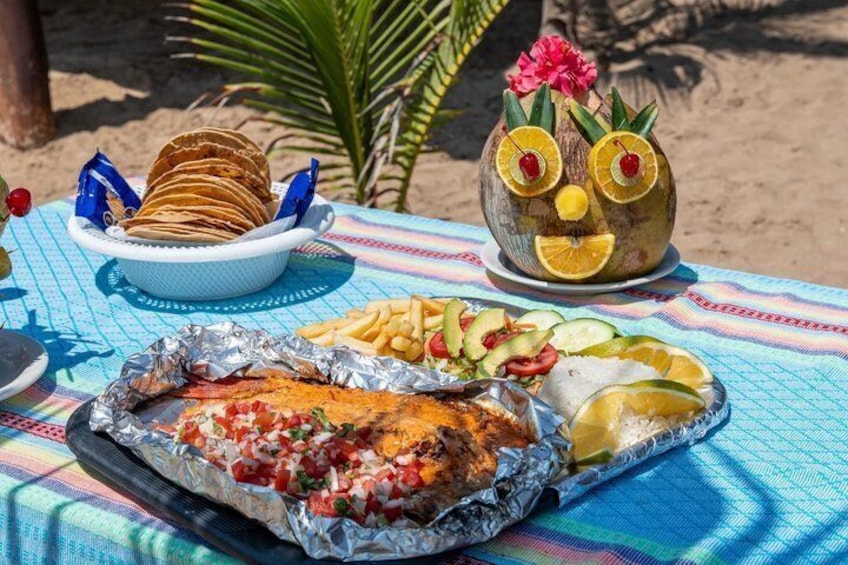 A beach picnic with grilled chicken, fries, and a decorative coconut. 3