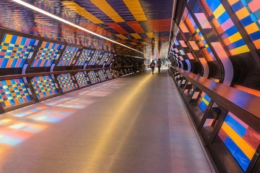 A brightly lit pedestrian bridge with colorful geometric patterns on the walls and ceiling. 5