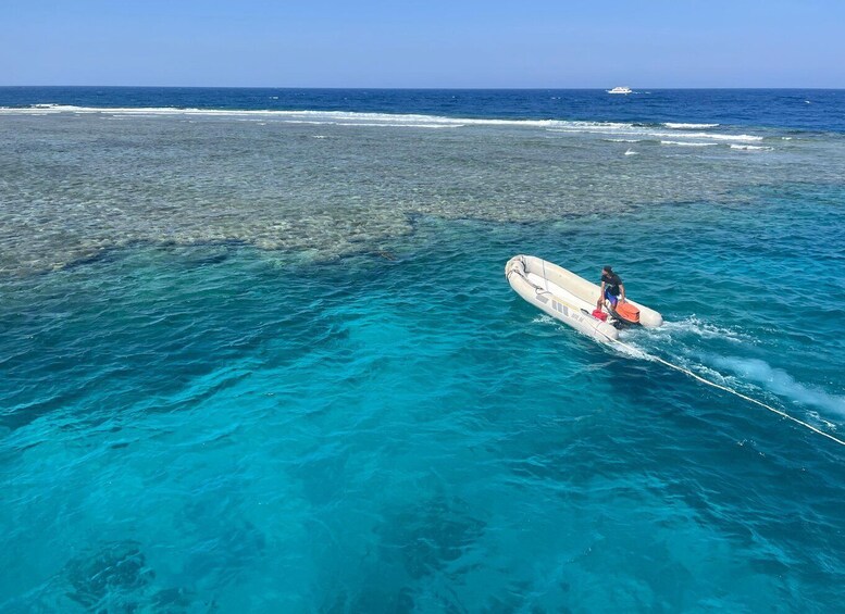 A person in a boat on clear blue water, with a distant shoreline and a boat in the background. 4