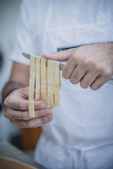 A person slicing a long, thin, yellowish food item with a knife. 5