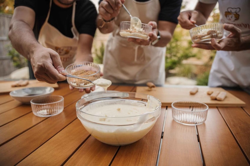 People preparing food outdoors, with a large mixing bowl and smaller bowls on a wooden table. 1