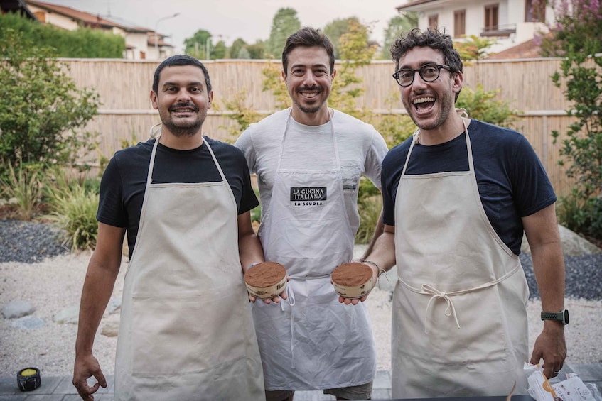 Three individuals wearing aprons, each holding a round object, standing outdoors with a wooden fence and greenery in the background. 2