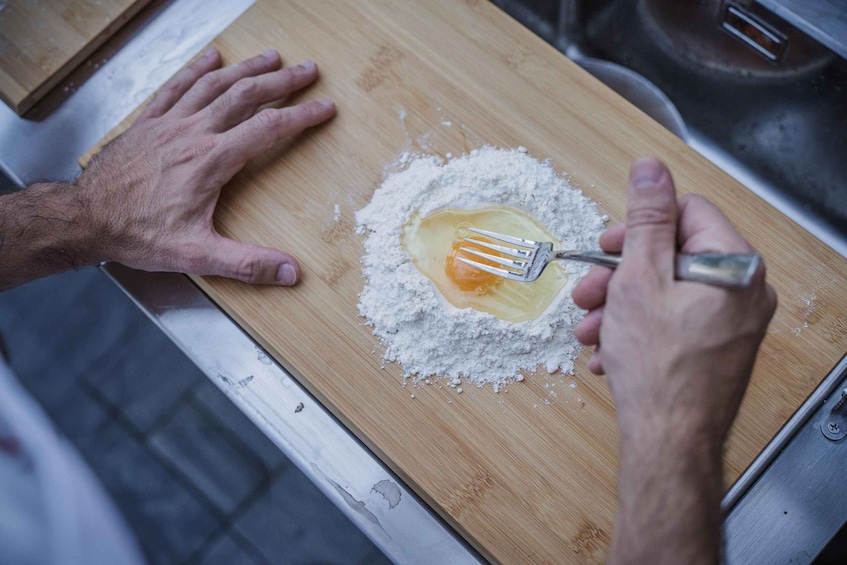 A person mixing an egg with flour on a wooden cutting board. 4