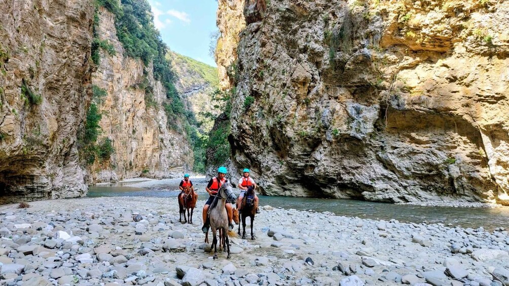A group of people on horseback in a rocky canyon with a river. 1
