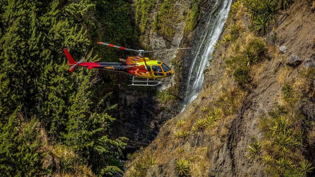 A helicopter flying over a waterfall surrounded by dense forest. 5